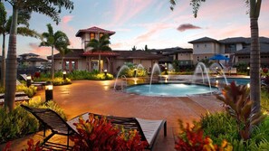 A pool area with a fountain, lounge chairs, and a building with a red roof. - Pili Mai - 5BR Townhomes - Sleeps 14 (Koloa)