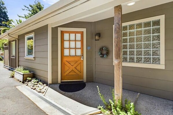 Una casa con puerta de madera, un pequeño porche con un felpudo negro y una ventana con diseño de cuadrícula.