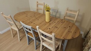Ein runder Holztisch mit sechs Stühlen, eine Vase mit gelben Blumen und eine helle Wand.