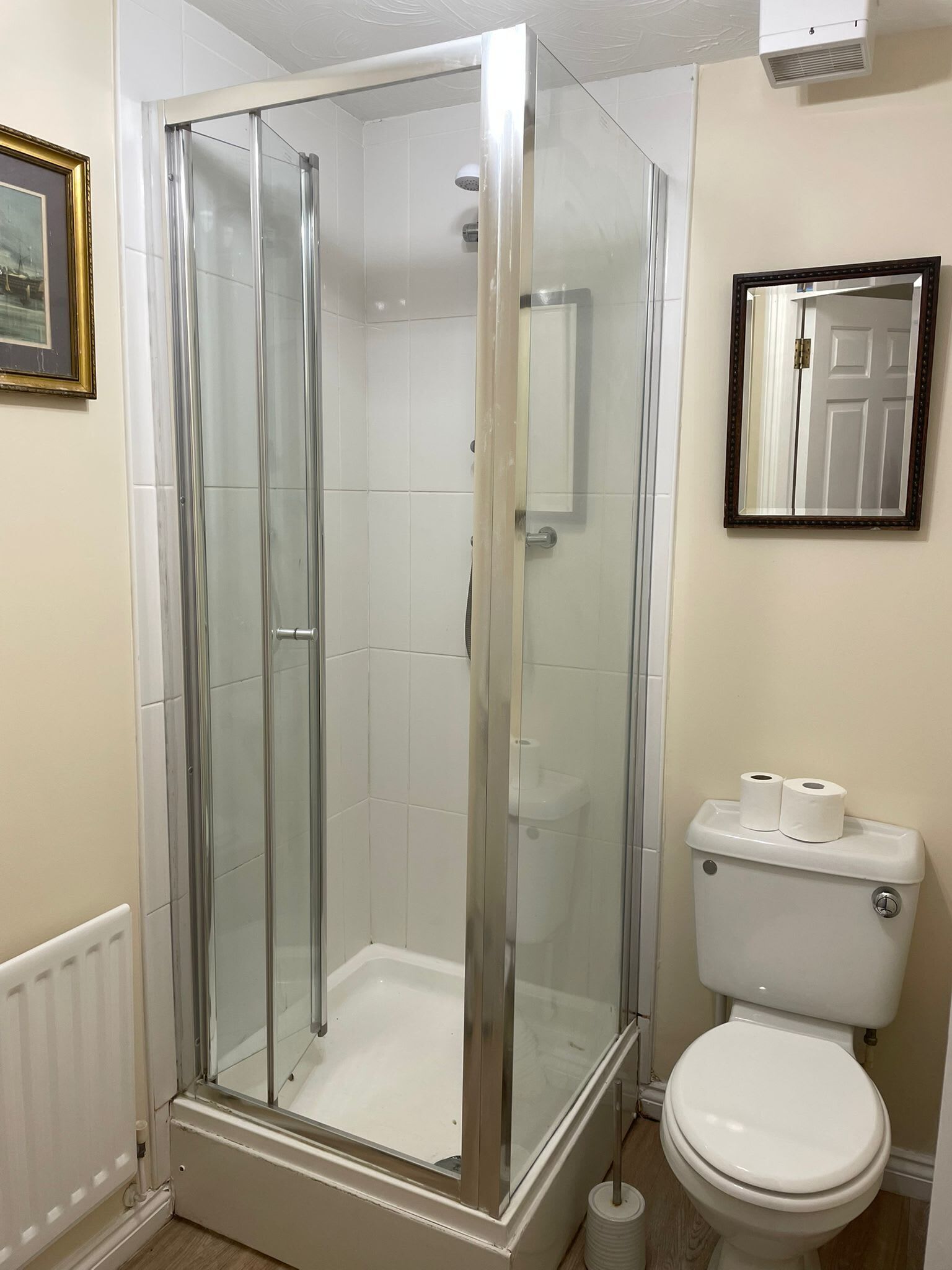 A bathroom with a glass-enclosed shower, a toilet, and a framed mirror.
