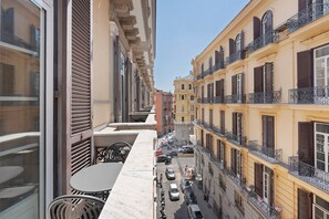 Eine enge Straße mit Gebäuden an beiden Seiten, Balkone mit schmiedeeisernen Geländern und ein Tisch mit Stühlen auf der linken Seite.