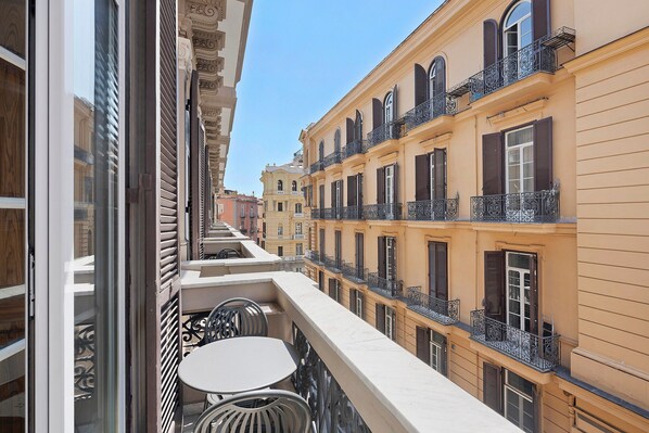 A narrow street with buildings on either side, a balcony with a table and chairs, and a clear blue sky. - Room 'Camera Tripla Superior' with Balcony, Wi-Fi and Air Conditioning (Napoli)