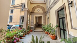 Ein schmaler Innenhof mit Blumentöpfen, einer Treppe zu einer oberen Etage und einem stehenden Auto.