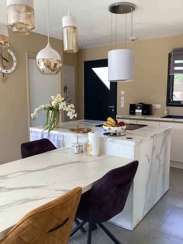 Une cuisine moderne dotée d’un îlot en marbre, de luminaires suspendus et d’un coin repas avec des chaises.