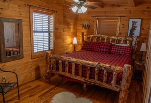 Ein Schlafzimmer einer Holzhütte mit einem Bett, einem Sessel, einem Fenster und einem Deckenventilator.