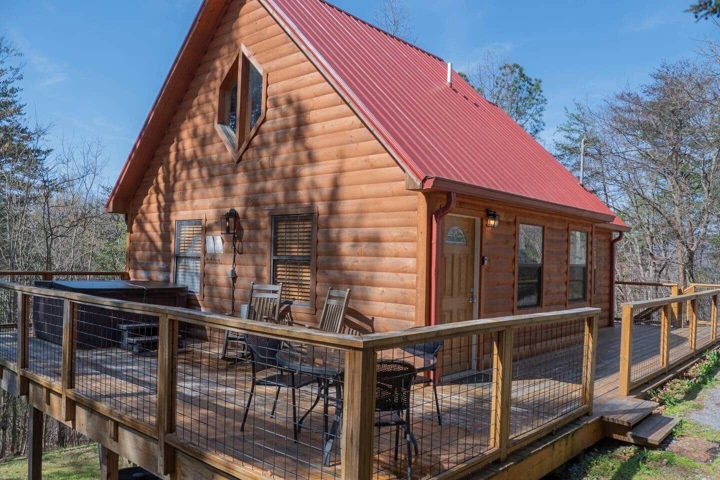 A log cabin with a red roof, a deck with chairs, and a small outdoor table.