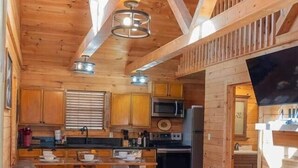 A wooden cabin interior with a living area, kitchen, and a fireplace. - Lazy Bear Den | Cozy w/ Hot Tub (Sevier County)
