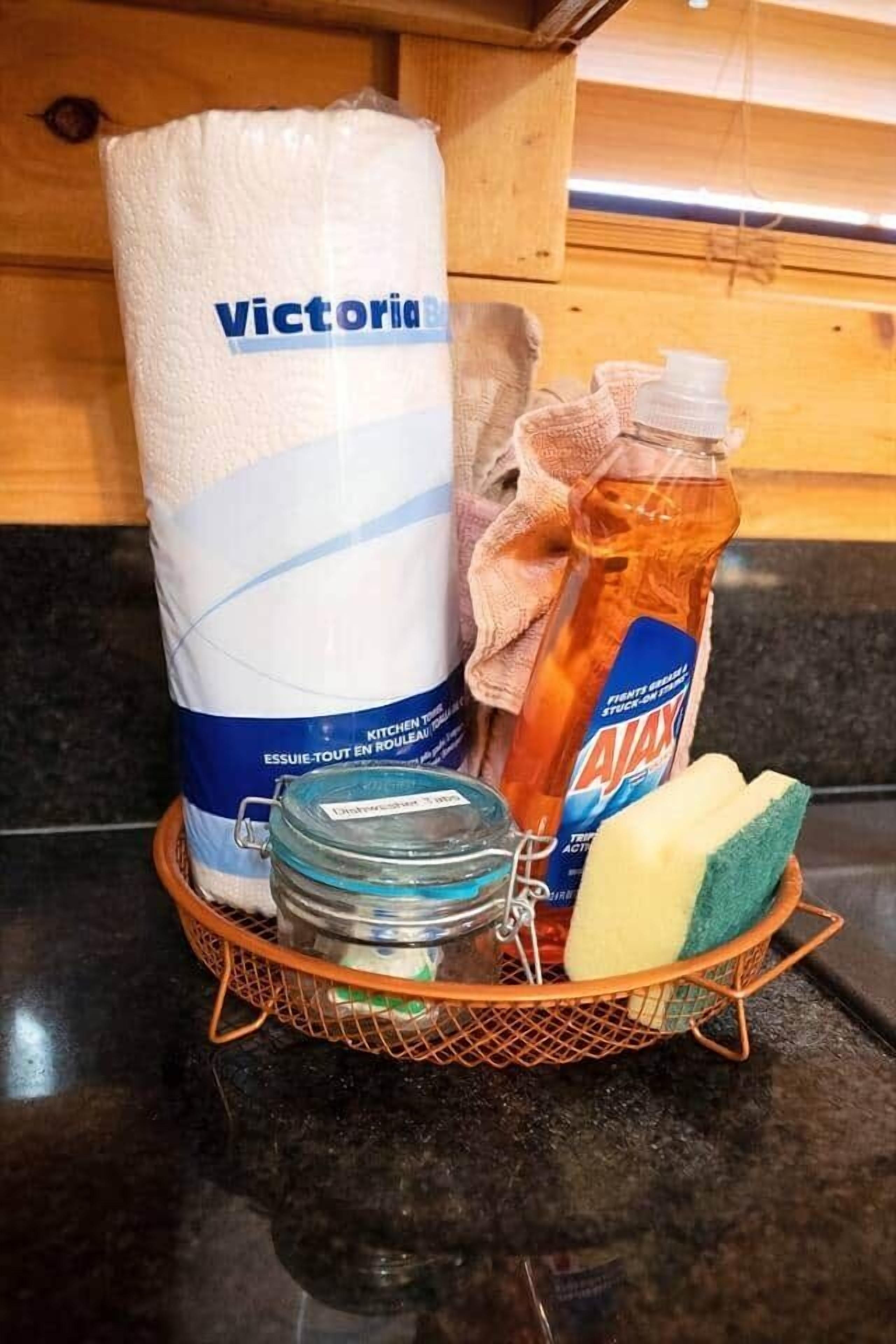 Een aanrecht met een rol keukenpapier, een fles Ajax afwasmiddel, een pot, een spons en een doek.
