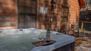 A hot tub with a bottle and glasses on a wooden deck, wooden walls, and a window with blinds. - Lazy Bear Den | Cozy w/ Hot Tub (Sevier County)