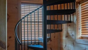 A spiral staircase in a wooden cabin with a window with blinds. - Lazy Bear Den | Cozy w/ Hot Tub (Sevier County)