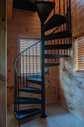 Een spiraaltrap in een houten hut met een raam voorzien van luiken.