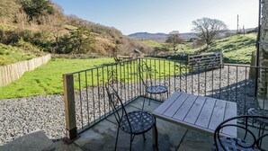 Un patio con tavolo e sedie, vista su un campo verde e un edificio in pietra.