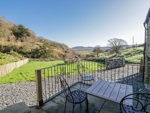 Eine Terrasse mit Tisch und Stühlen, Blick auf ein grünes Feld und ein Steinhaus.