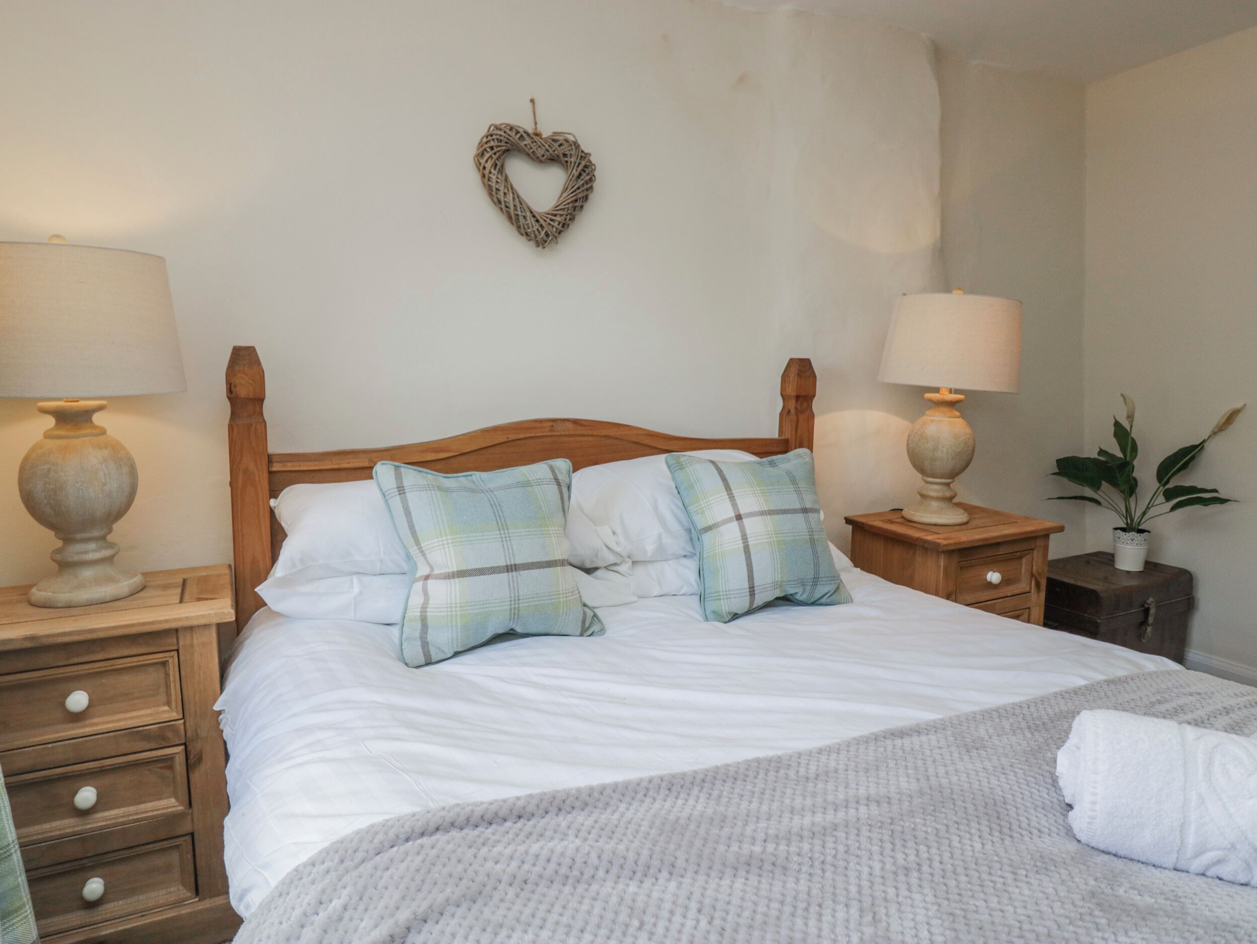 A neatly made bed with two pillows, a heart-shaped decoration on the wall, and two bedside tables with lamps.