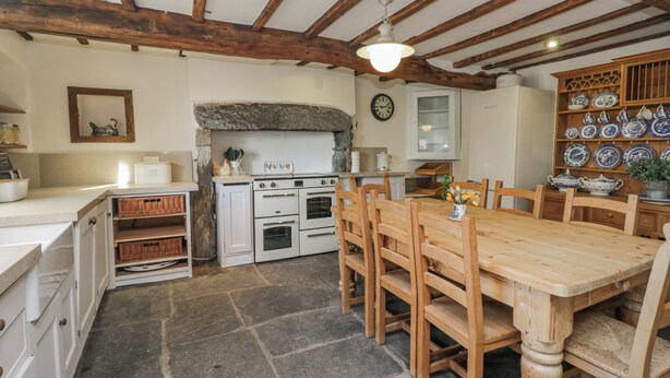Una cucina rustica con pavimento in pietra, travi in legno, un grande stufa e un tavolo da pranzo con sedie.