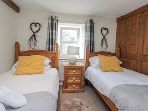 A room with two wooden beds, a window with curtains, a nightstand with a lamp, and heart-shaped wall decorations. - High Ickenthwaite Farmhouse (Ulverston)