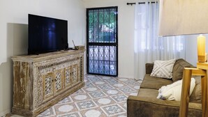 Un salon avec un téléviseur posé sur un meuble en bois, un canapé marron et une porte surmontée d’un portail en métal.