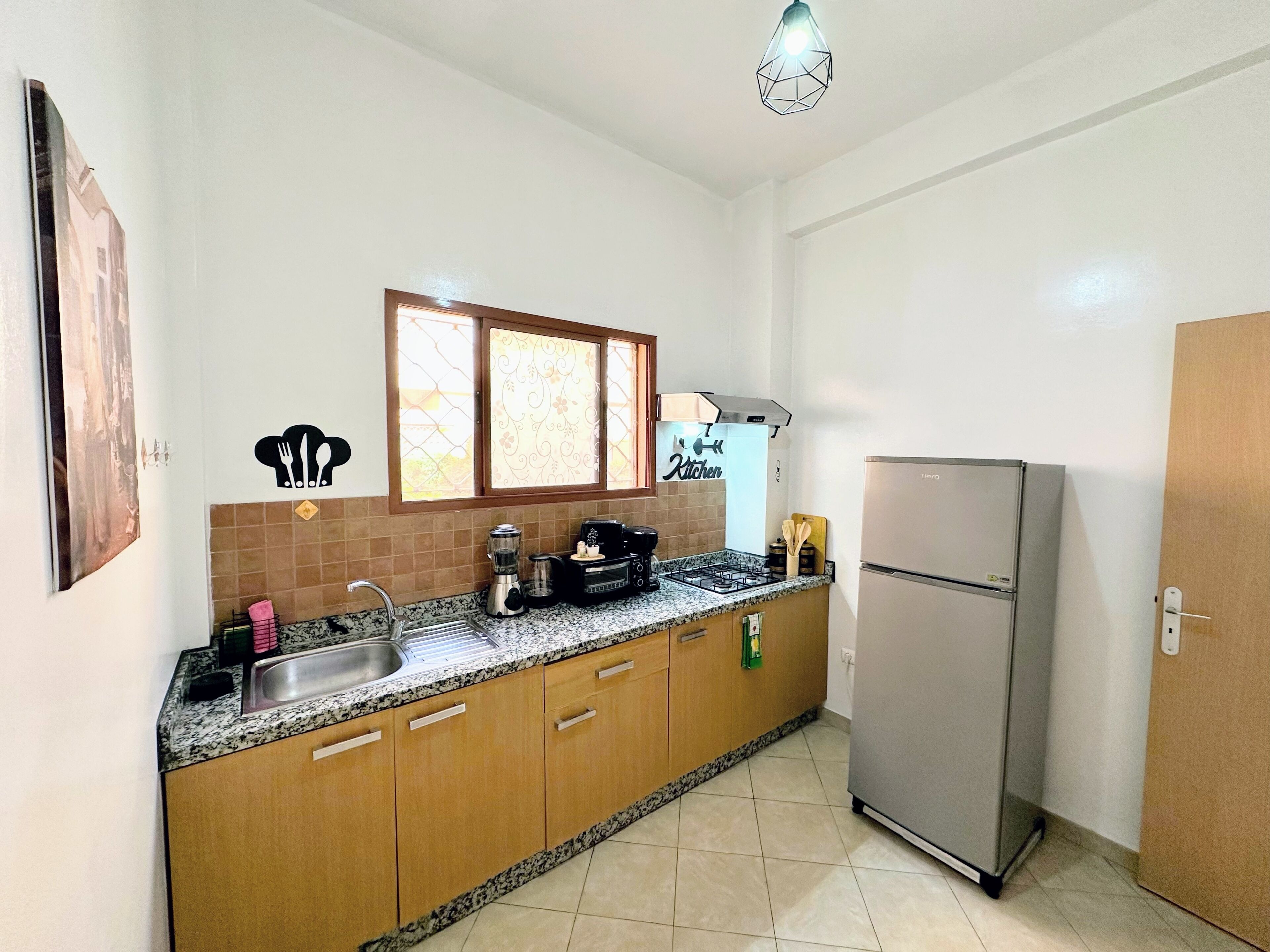 A kitchen with a sink, stove, refrigerator, and a window with decorative curtains.