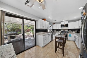A modern kitchen with white cabinets, a large island, and a sliding glass door leading to an outdoor area. - Cozy 3BR Retreat w/ Spa in Green Valley Area (Henderson)