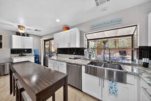 A modern kitchen with white cabinets, a marble countertop, a stainless steel sink, and a dining area with a wooden table. - Cozy 3BR Retreat w/ Spa in Green Valley Area (Henderson)