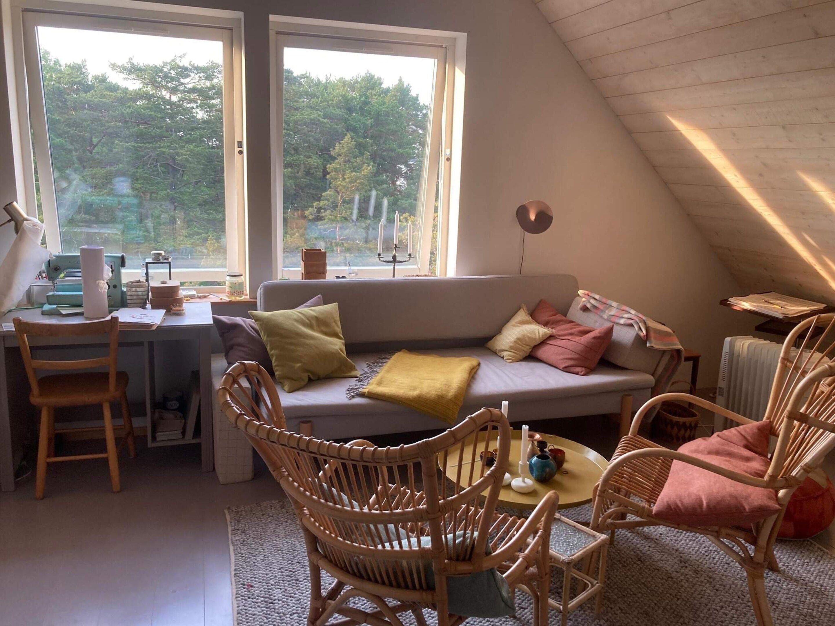 Una habitación acogedora con techo a la altura de un loft, un sofá con cojines, una mesa de comedor con sillas y una máquina de coser sobre un escritorio.