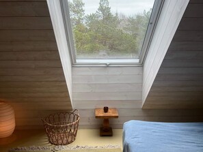 A room with a sloped ceiling, a small wooden table with a candle, a wicker basket, and a bed with a blue cover. - 4 Star Holiday Home in Runmaro (Runmaro)