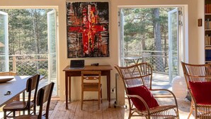 A room with a dining table, chairs, a laptop on a desk, a large abstract painting, and a view of trees through open doors. - 4 Star Holiday Home in Runmaro (Runmaro)