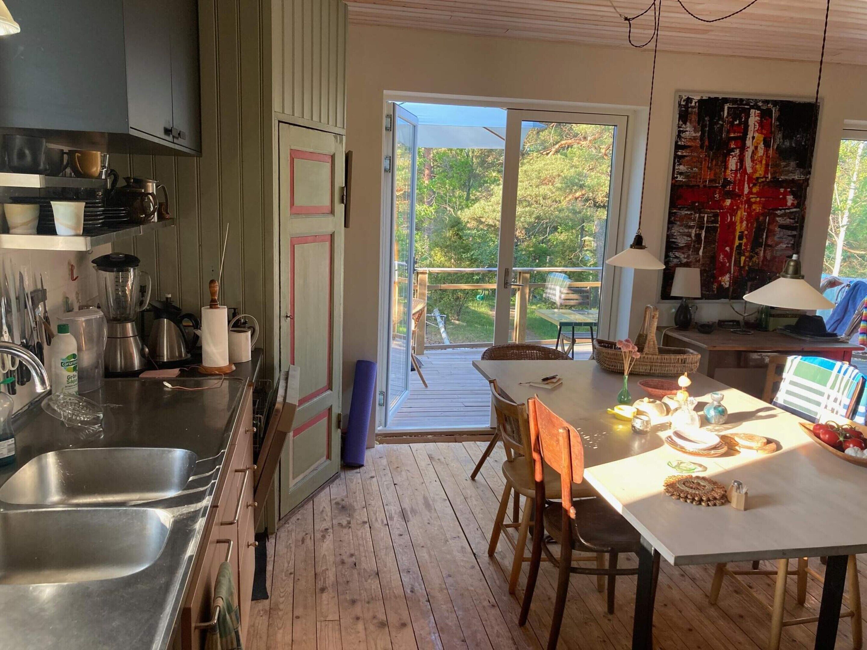 Una cocina con un ventanal grande, un comedor con mesa y sillas, y un balcón con vistas a árboles.