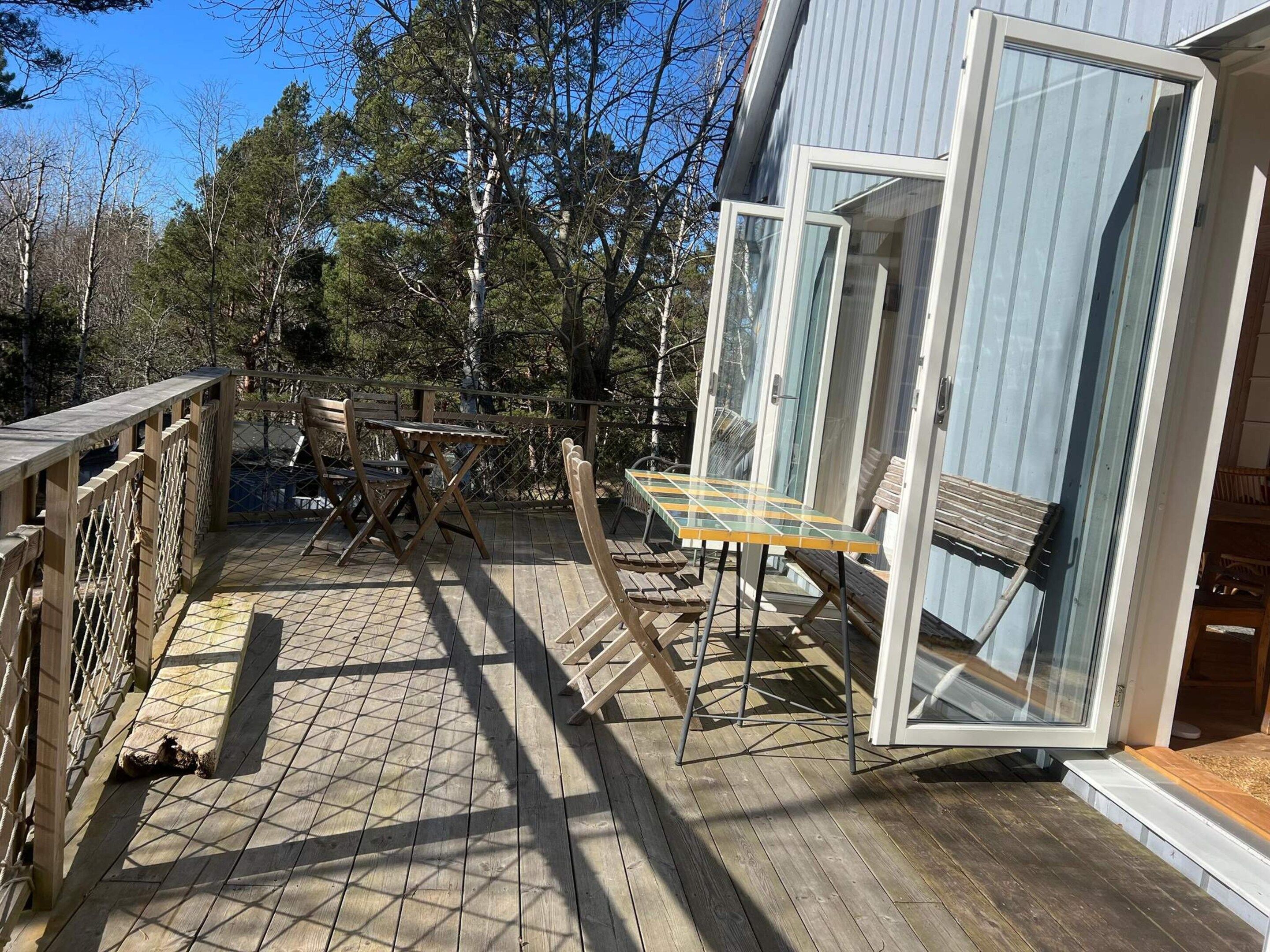 Eine Holzterrasse mit Tisch, Stühlen, einer Glastür und einem Metallgeländer.