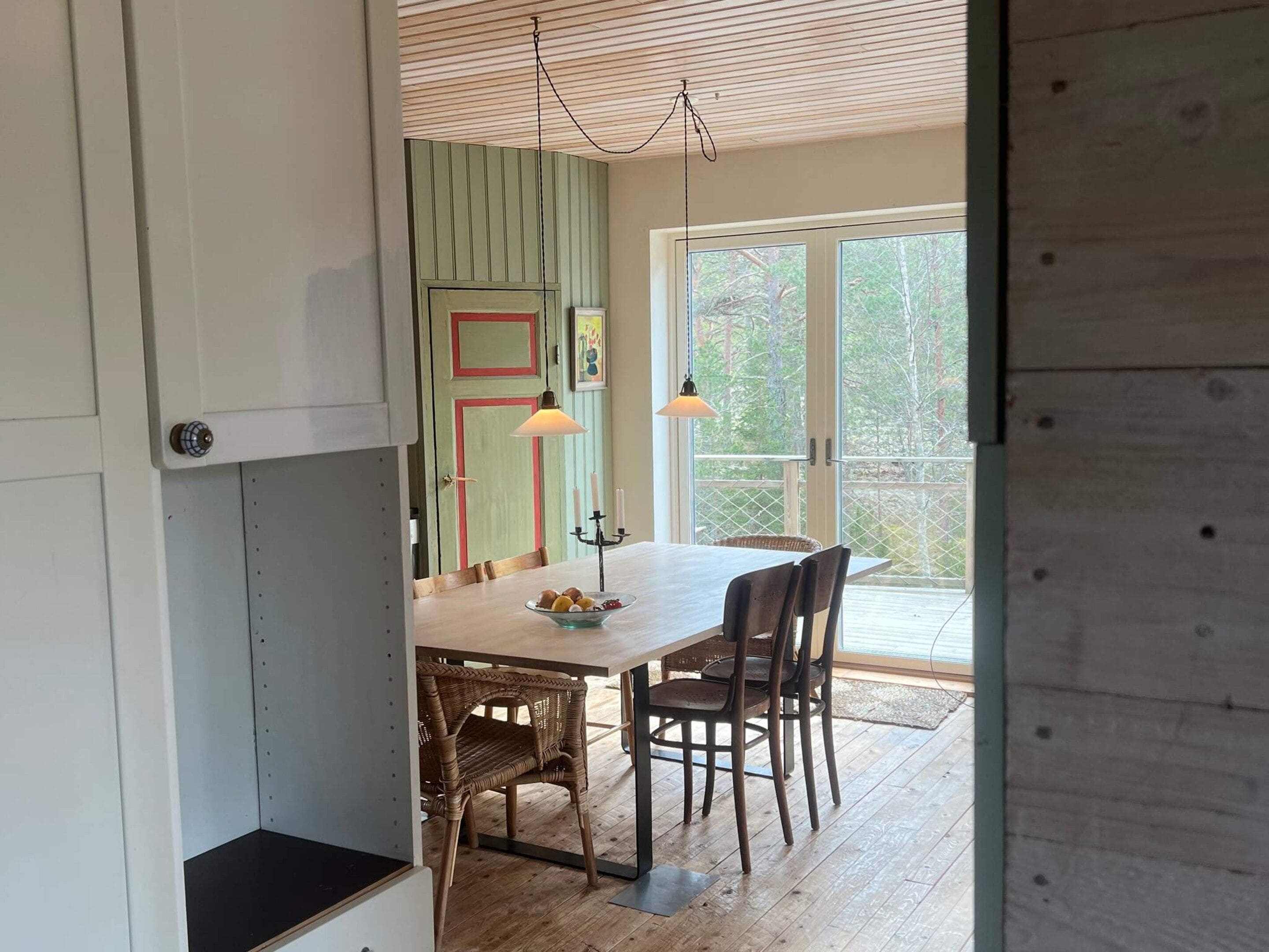 Comedor con mesa de madera, sillas de mimbre y vistas al exterior a través de un ventanal.