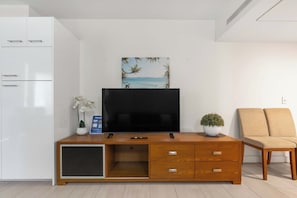 Un salon moderne avec un téléviseur à écran plat, un meuble de rangement en bois doté de tiroirs, une petite plante en pot et un canapé beige.