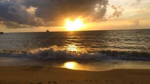A beach with the sun setting over the ocean, waves crashing onto the shore, and a pier in the distance. - Drift into Paradise: Exceptional Resort Living (Palm Cove)