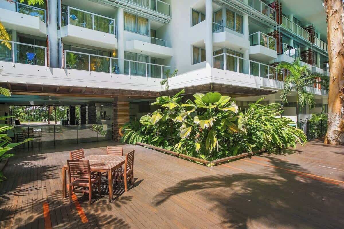 Een modern hotel met meerdere balkons, een centrale binnenplaats met tropische planten en zitplaatsen buiten.