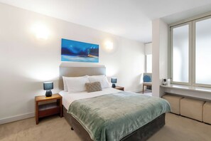 Une chambre moderne avec un grand lit, deux tables de chevet, une commode, une fenêtre avec des stores et un tableau au mur.