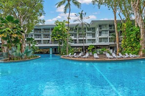 Ein Hotel mit Swimmingpool, umgeben von Palmen und Liegestühlen.