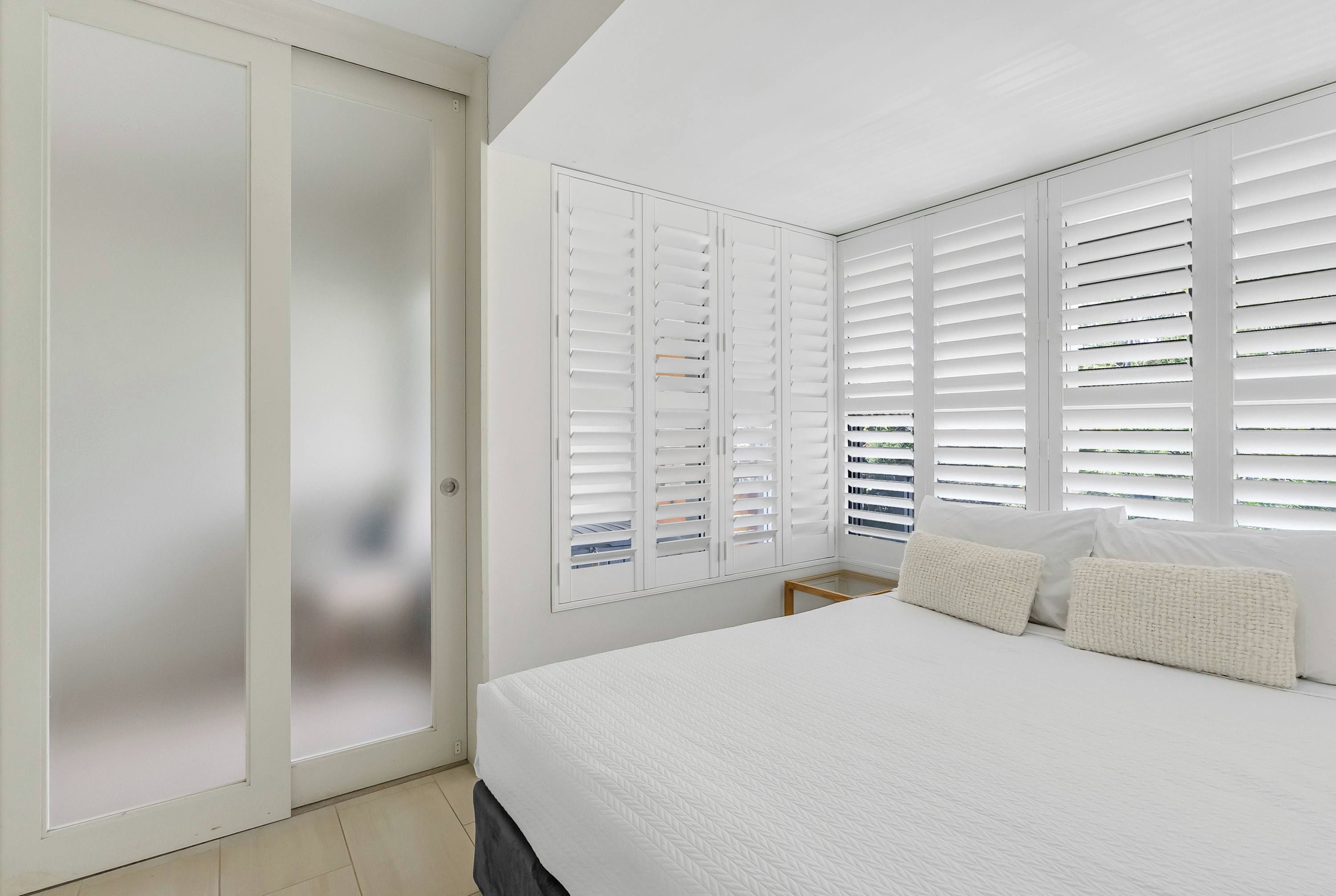 A bedroom with a bed, a wardrobe, and a window with blinds.