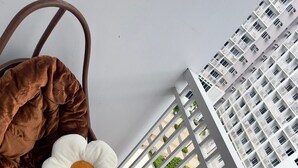 Udsigt fra en balkon med en vævet måtte, en hvid blomst og en brun taske.