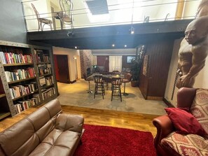 A living room with a leather sofa, a red rug, a dining area with a table and chairs, and a bookshelf filled with books. - Cosy American Style apartment (Liverpool)