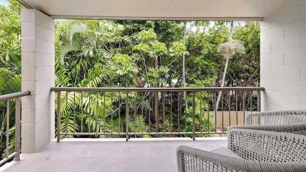 Un balcone con vista su una vegetazione lussureggiante, una ringhiera in metallo e mobili in vimini.