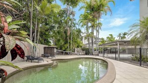 Una piscina a bordo curvo, circondata da una recinzione, adiacente a un edificio con un patio coperto.
