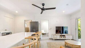 Una cucina moderna con isola centrale, sgabelli da bar, una ventola a soffitto e una TV nella zona living.