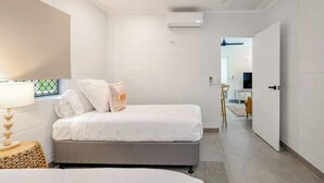 Una camera da letto con un letto, una lampada da comodino, un condizionatore d'aria a parete e una porta che dà su un'altra stanza.