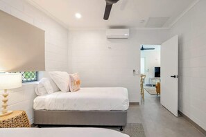 Ein Schlafzimmer mit einem Bett, einer Nachttischlampe, einer Wand-Klimaanlage und einer Tür zu einem anderen Raum.
