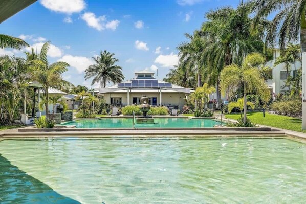 Un complexe hôtelier doté d’une piscine, de palmiers et d’un bâtiment équipé de panneaux solaires.