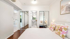 A bedroom with a large bed, a desk, and a bathroom visible through an open door. - Trinity Beach Bliss: Experience Tropical Living (Trinity Beach)