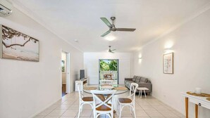 A dining area with a round table, white chairs, ceiling fans, and a view of a garden through a window. - Trinity Beach Bliss: Experience Tropical Living (Trinity Beach)