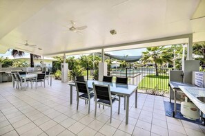 Une terrasse extérieure dotée d’un espace salon couvert, d’un coin barbecue et offrant une vue sur une piscine et un espace verdoyant.