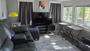 Una sala de estar con un sofá seccional, un televisor de pantalla plana, un ventilador de techo y un ventanal grande.