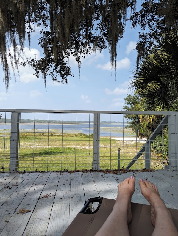 A wooden deck with a railing, overlooking a grassy area and a body of water.