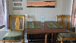 Un comedor con una mesa de madera, dos sillas con cojines verdes, un jarrón decorativo y un cartel en la pared con frases motivacionales.